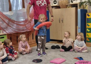 Trener prezentuje dzieciom jak należy prawidłowo trzymać makaron do pływania.