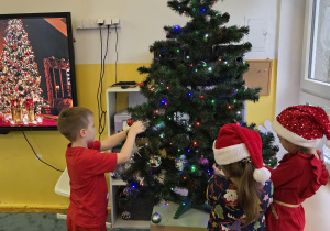 Dzieci zakładają na choinkę piękne bombki.