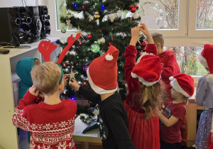 Dzieci wspólnie ubierają choinkę.