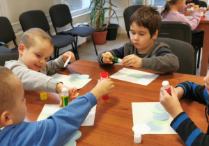 Chłopcy naklejają koła na kartkę.