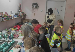 Dzieci oglądają jak wygląda ręczne dekorowanie bombek.