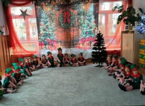 Dzieci w strojach elfów siedzą na dywanie w dużym półkolu.