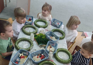 Dzieci siedzą przy stolikach na których leżą przygotowane materiały do pracy.