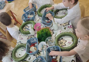 Dzieci oglądają elementy zdobnicze umieszczone w koszyczkach ustawionych na stole.