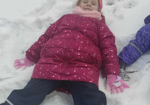 Dziewczynka robi "aniołka" na śniegu.
