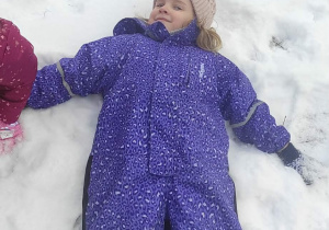 Dziewczynka robi "aniołka" na śniegu.