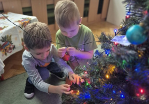 Dzieci wieszają bombki na choince.