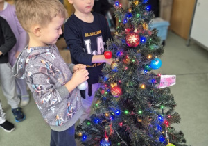 Chłopcy ubierają wspólnie choinkę.