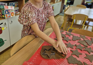 Dziewczynka z wielkim skupieniem wycina pierniki z rozwałkowanego ciasta.