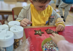 Chłopiec z wielkim zaangażowaniem dekoruje pierniki.
