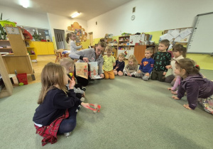 Dzieci siedzą na dywanie i z zaciekawieniem oglądają książkę.