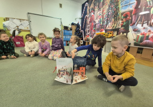 Dzieci siedzą na dywanie i oglądają książkę.