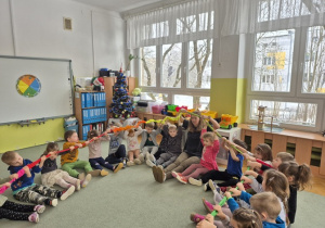 Na dywanie panuje radosna atmosfera, a dzieci cieszą się zabawą z kolorową gumą sensoryczną.