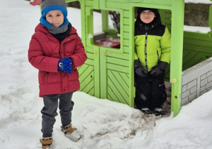 Dzieci w ogrodzie przedszkolnym bawią się na śniegu.