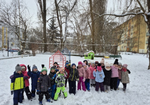 Dzieci wspólnie stoją na śniegu na dworze, uśmiechając się do zdjęcia w radosnej, zimowej atmosferze.