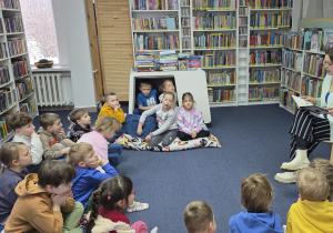 Dzieci słuchają książki czytanej przez Panią bibliotekarkę.