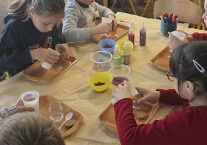 Dzieci przygotowują naturalne dyfuzory zapachowe - na początek nalewają wody do małych słoiczków.