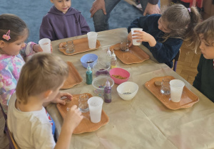 Pan prowadzący pomaga dzieciom odmierzyć odpowiednią ilość wody w słoiczkach.