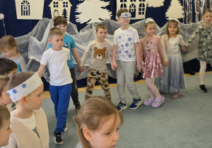 Dzieci trzymają się za ręce i idą po obwodzie koła w rytmie zimowej piosenki.