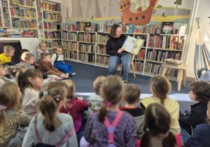 Pani czyta dzieciom książkę o dinozaurach.