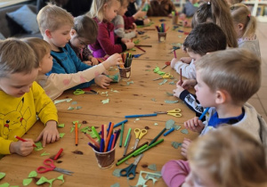 Dzieci stoją przy stole i wykonują swoje dinozaury.
