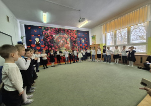 Dzieci stoją w półkolu i śpiewają piosenkę.