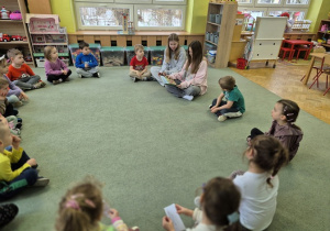Starsze koleżanki siedzą z dziećmi na dywanie i czytają im opowiadanie o Kubusiu Puchatku..