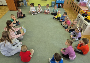 Dzieci siedzą na dywanie i uważnie słuchają.