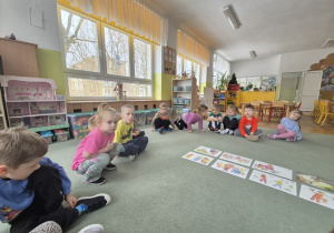 Dzieci siedzą na dywanie w kole i uważnie słuchają czytanego przez nauczyciela opowiadania.