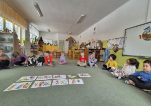 Dzieci siedzą na dywanie i przyglądają się ilustracją do opowiadania.