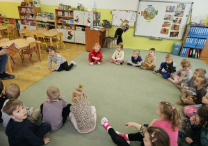 Dzieci siedzą na dywanie w kole i czekają na czytanie opowiadania.