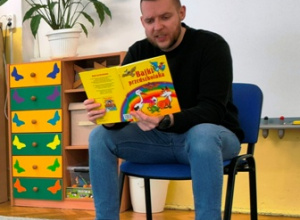 Mężczyzna siedzący na krześle czyta bajkę dzieciom.