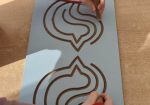 Dziecko przesuwa oburącz drewniane pisaki po wzorze.