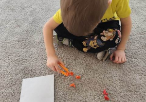 Chłopiec przenosi bibułowe kuleczki na kartkę za pomocą plastikowej pęsety.