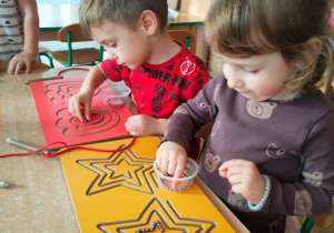 Dzieci układają koraliki w rowkach tablicy grafomotorycznej- stosują chwyt pęsetowy.