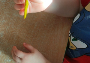 Dziecko wałkuje plastelinę w paluszkach jednej dłoni.