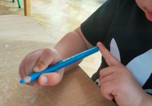 Dziecko uczy się prawidłowego trzymania przyboru- chwytu pisarskiego.