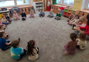 Dzieci wraz z gościem siedzą w dużym kole na dywanie.