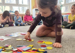 Dziewczynka wybiera wskazane opisem figury i układa je zgodnie z poleceniami nauczyciela.