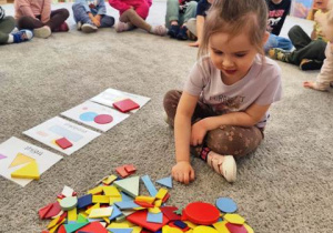 Dziewczynka szuka figur określonej wielkości i układa je na planszach edukacyjnych.