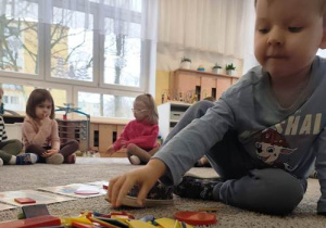 Chłopiec wybiera spośród figur tę, która odpowiada opisowi słownemu nauczyciela.