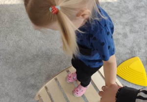 Dziecko z pomocą nauczyciela pokonuje przeszkodę- idzie po drabince montessori.