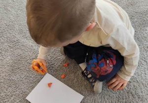 Dziecko przenosi za pomocą pęsety kuleczki bibułowe na kartkę papieru.