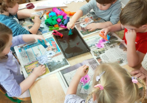 Dzieci kolorują dinusie stemplując papierową sylwetę kulkami krepiny namoczonymi w wodzie.