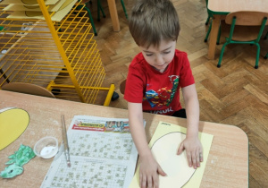 Chłopiec nakleja jajo na karton z dinozaurem.