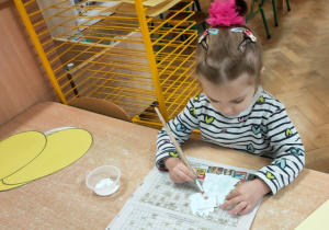 Dziewczynka smaruje klejem swojego dinozaura, by móc go potem przykleić do kartonu