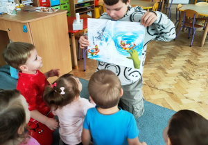 Chłopiec rozmawia z dziećmi, pyta je co widzą na obrazku.