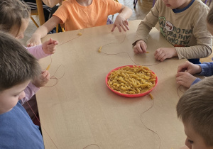 Dzieci wykonują makaronowy naszyjnik.