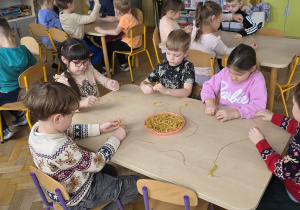 Dzieci wykonują makaronowy naszyjnik.
