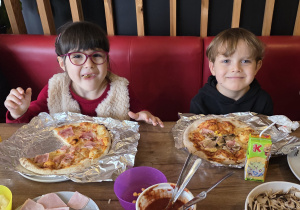 Dzieci jedzą przygotowane samodzielnie pizze.
